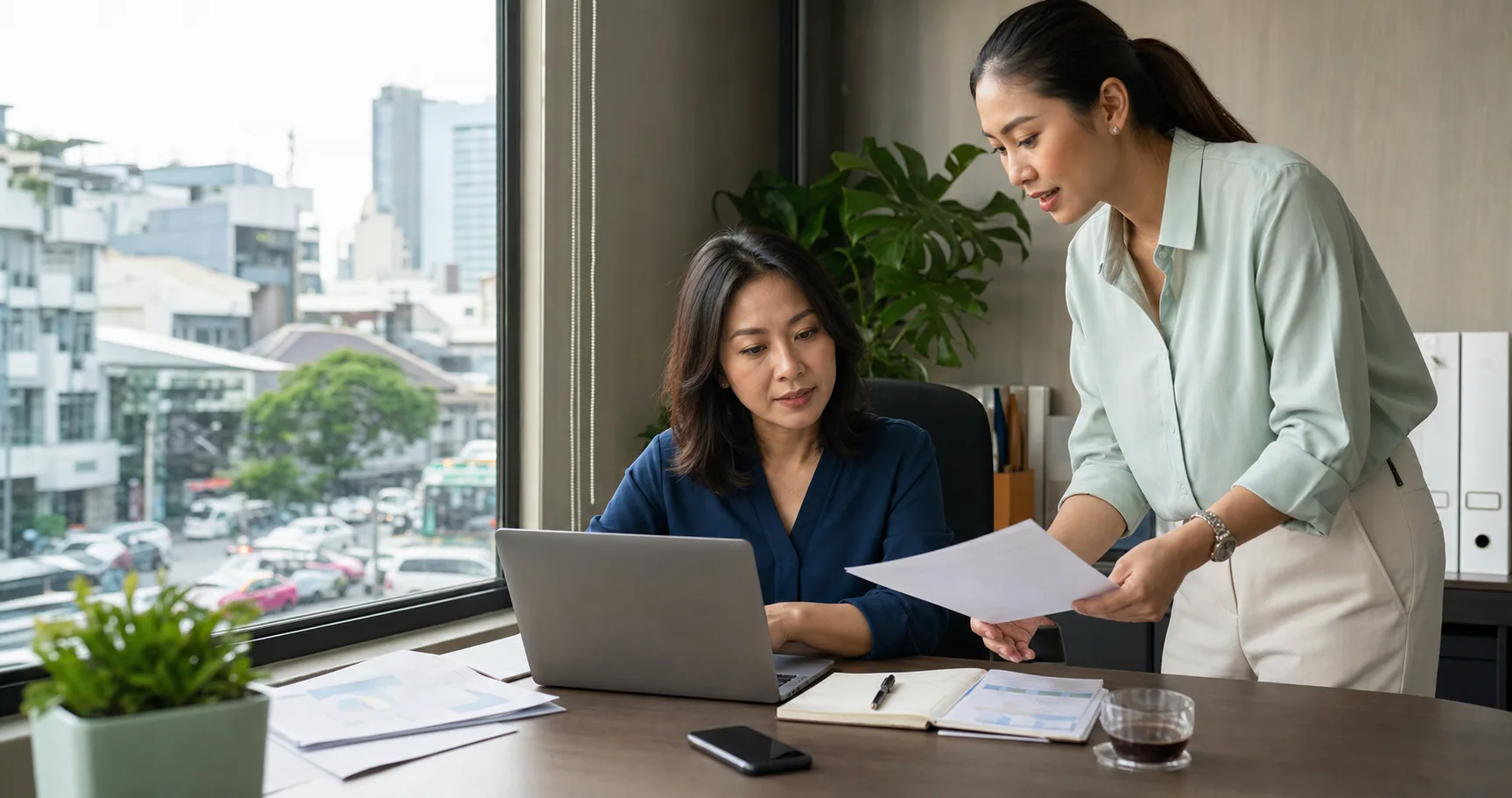 Two Thai business professionals reviewing work together in a Bangkok office